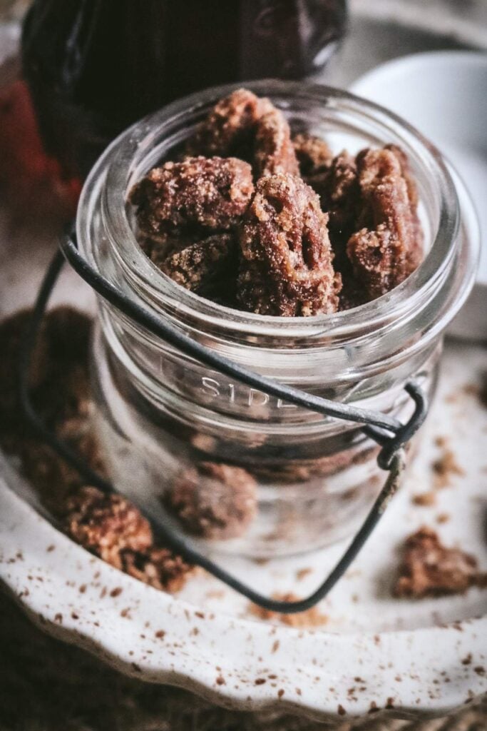 close up view of sugary candied pecans with maple glaze on a pie plate.
