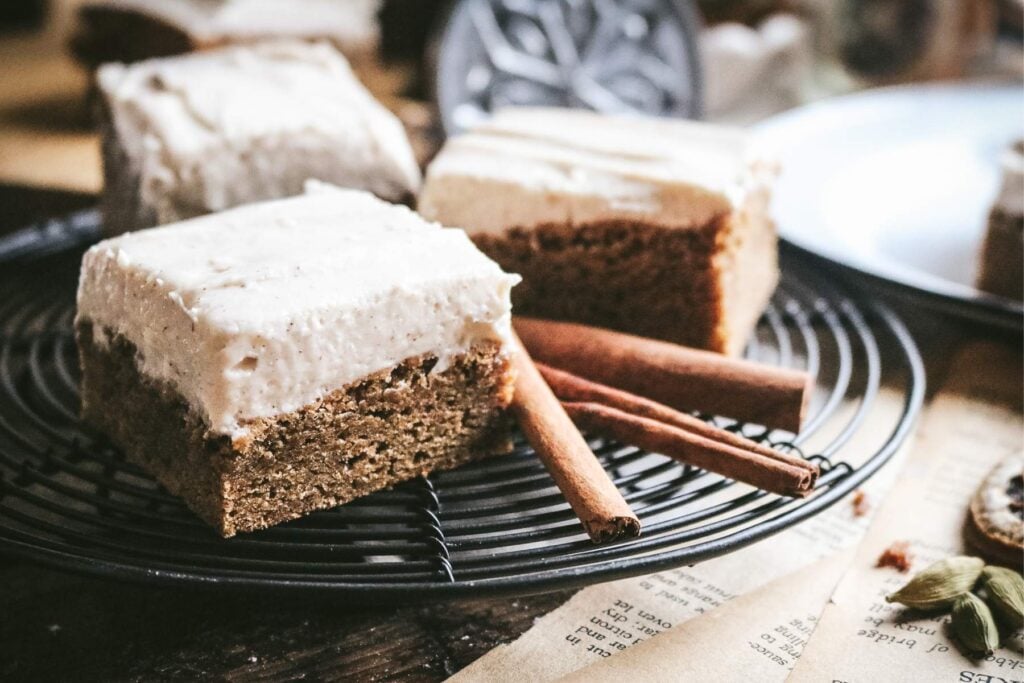 close up view of a frosted gingerbread blondie with creamy cinnamon cream cheese frosting next to cinnamon sticks and cardamom pods.