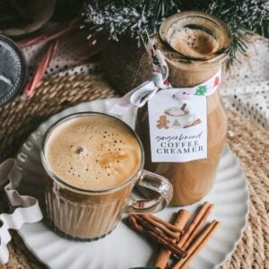 close up view of a glass mug with coffee and a bottle of gingerbread creamer with cinnamon sticks and a christmas tree.