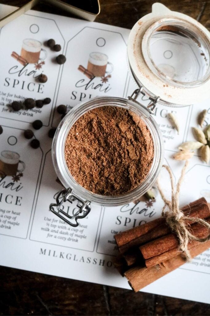 overhead view of a jar of homemade chai spice over printed labels next to lots of dried spices.