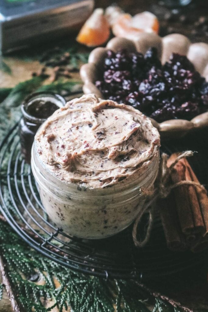 a close up view of a mason jar with thick, creamy spiced cranberry butter with dried cranberries in the back and cedar underneath.