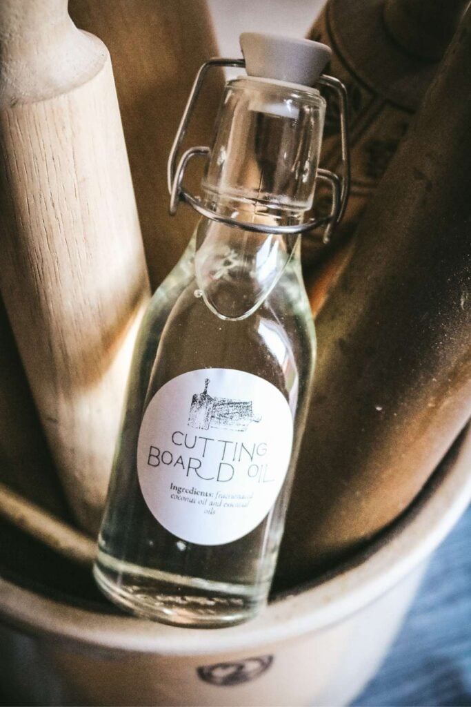 glass bottle of homemade cutting board oil sitting on wooden rolling pins.