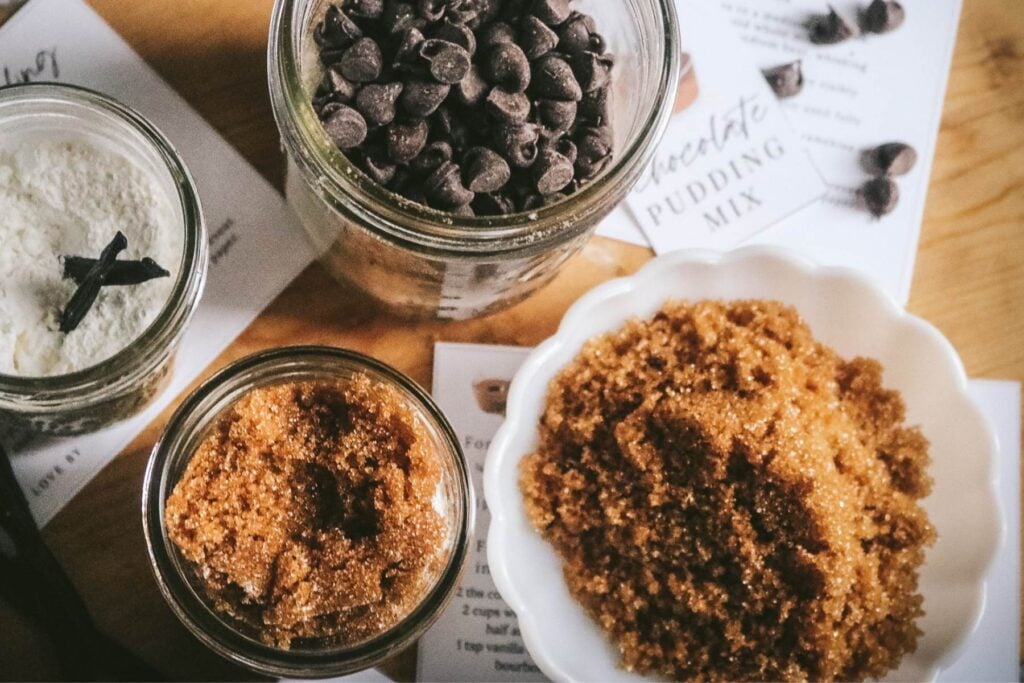 overhead view of a mason jar with butterscotch pudding mix, chocolate pudding mix, and vanilla bean pudding mix next to printable labels and recipe cards.