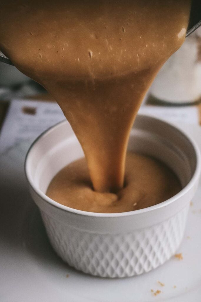 pouring butterscotch pudding made from scratch into a white ramekin.