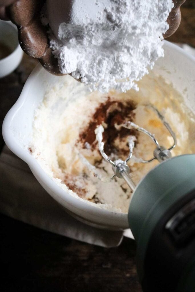 adding cinnamon, vanilla, and powdered sugar to cream cheese frosting.