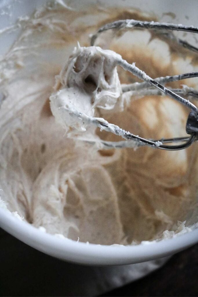 thick and fluffy cinnamon cream cheese frosting in a mixing bowl with beaters.