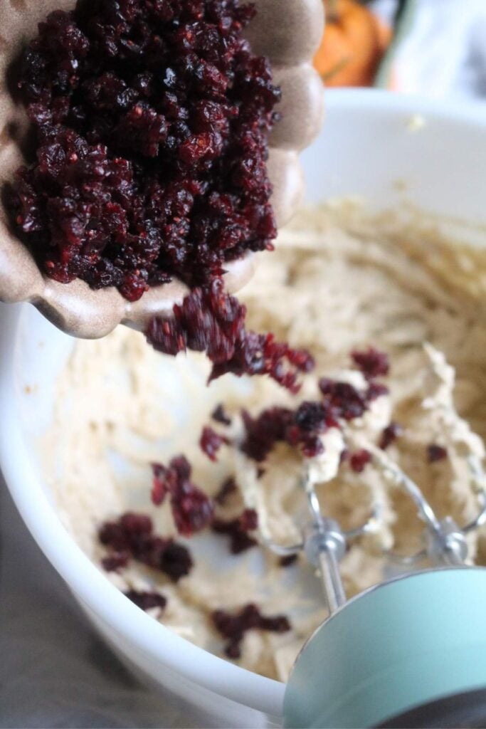 pouring minced dried cranberries into a bowl of whipped, spiced butter for cranberry butter.