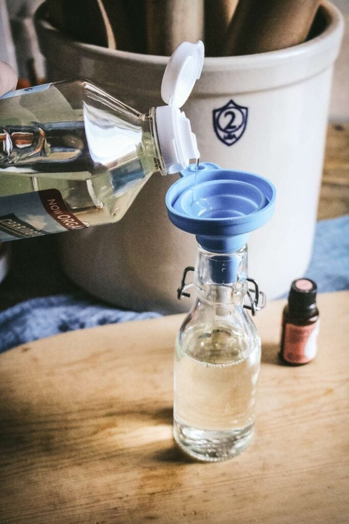 pouring fractionated coconut oil into a glass bottle to make homemade cutting board oil.