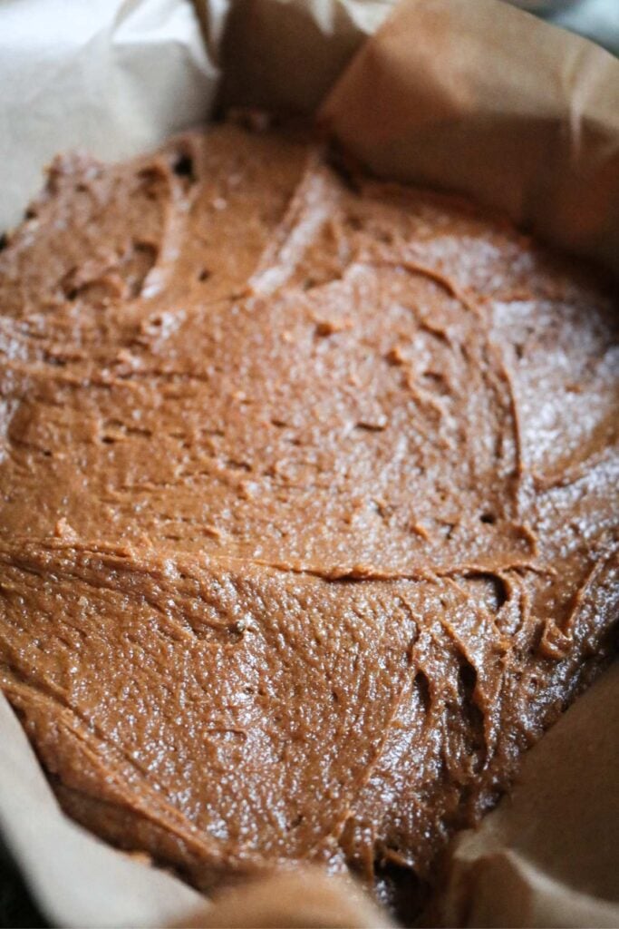 a square metal baking pan lined with parchment holding gingerbread blondie batter.