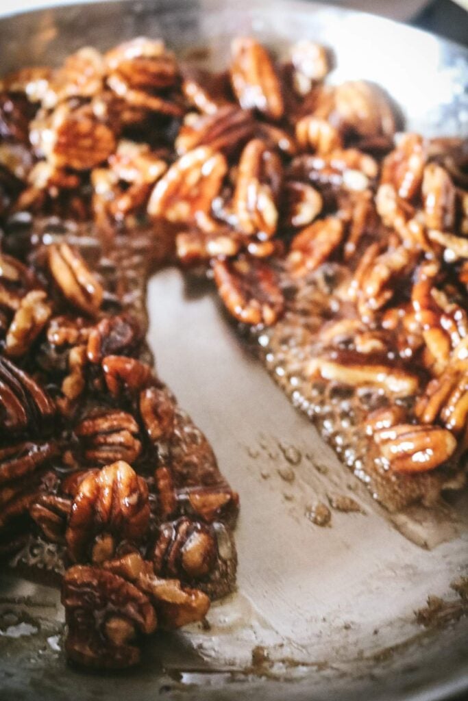 running a spatula down the center of a skillet to show how thick and evaporated the maple syrup is when making candied pecans.