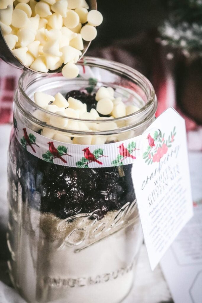 adding white chocolate chips to homemade muffin mix in a jar.