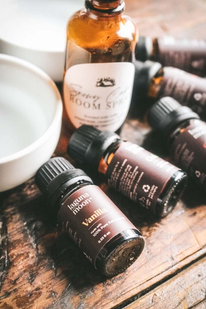 bottles of essential oils on a wooden table next to water and vodka and a spray bottle.