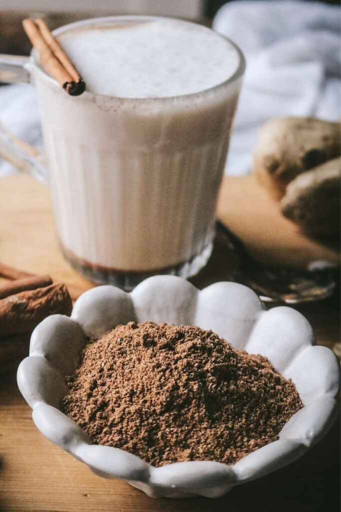 small white dish with homemade chai spice mix and a mug of maple chai in the back.