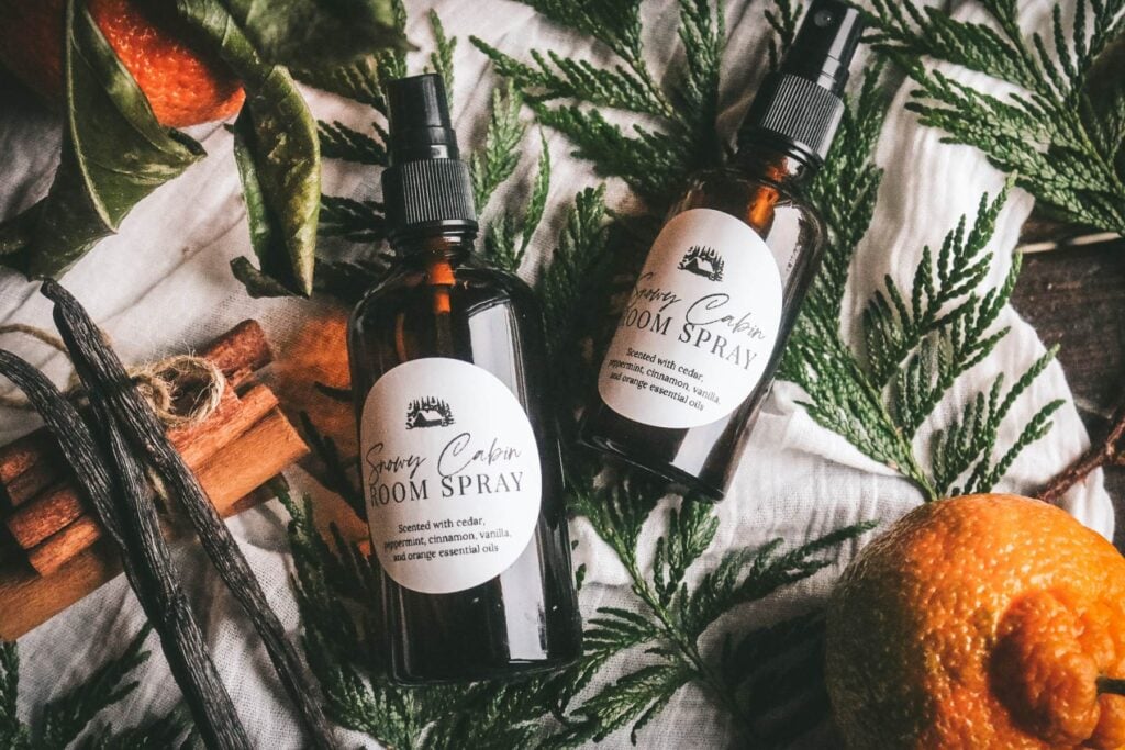 two bottles of winter room spray on a wooden table with cedar, vanilla bean, cinnamon sticks, and orange.