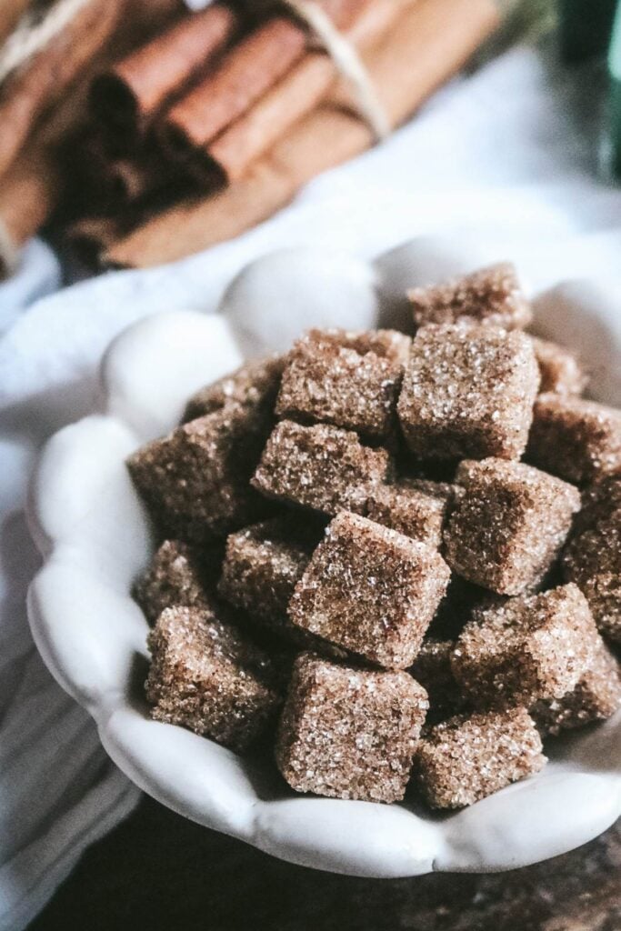 white scalloped bowl with homemade snickerdoodle flavored sugar cubes with cinnamon sticks in the background.