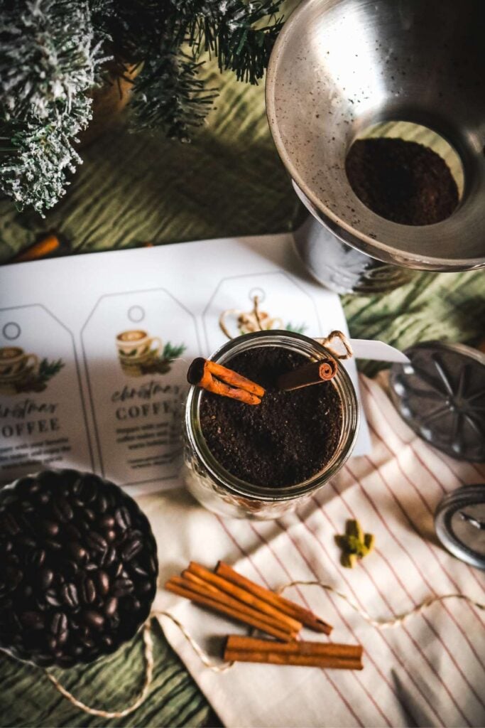 overhead view of a mason jar with cinnamon spiced coffee for christmas next to a second jar, printable labels, twine, coffee beans, and cinnamon sticks.