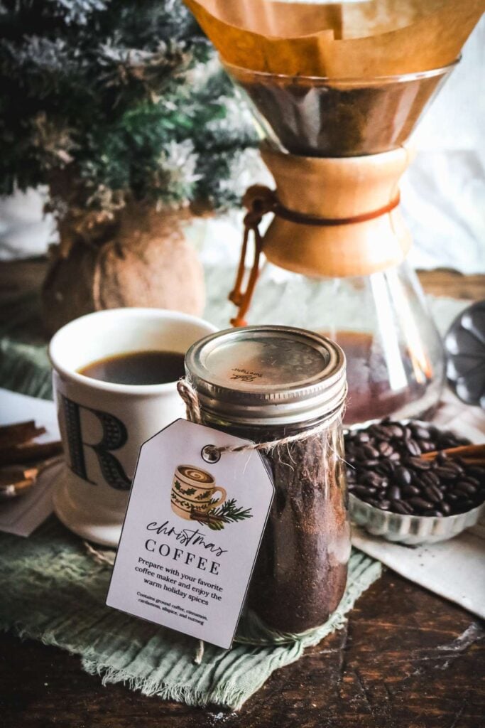 a glass jar with christmas coffee in front of a chemex and a mug of coffee with a christmas tree in the background.