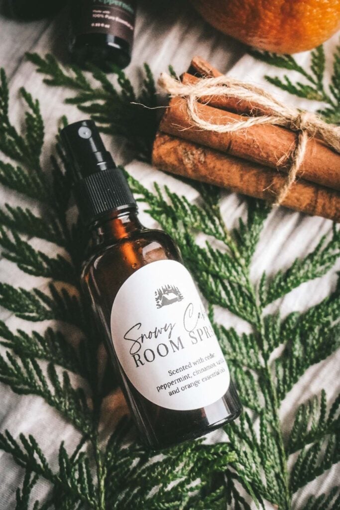 amber glass spray bottle with a homemade room spray for christmas next to cedar, cinnamon, orange, and essential oils.
