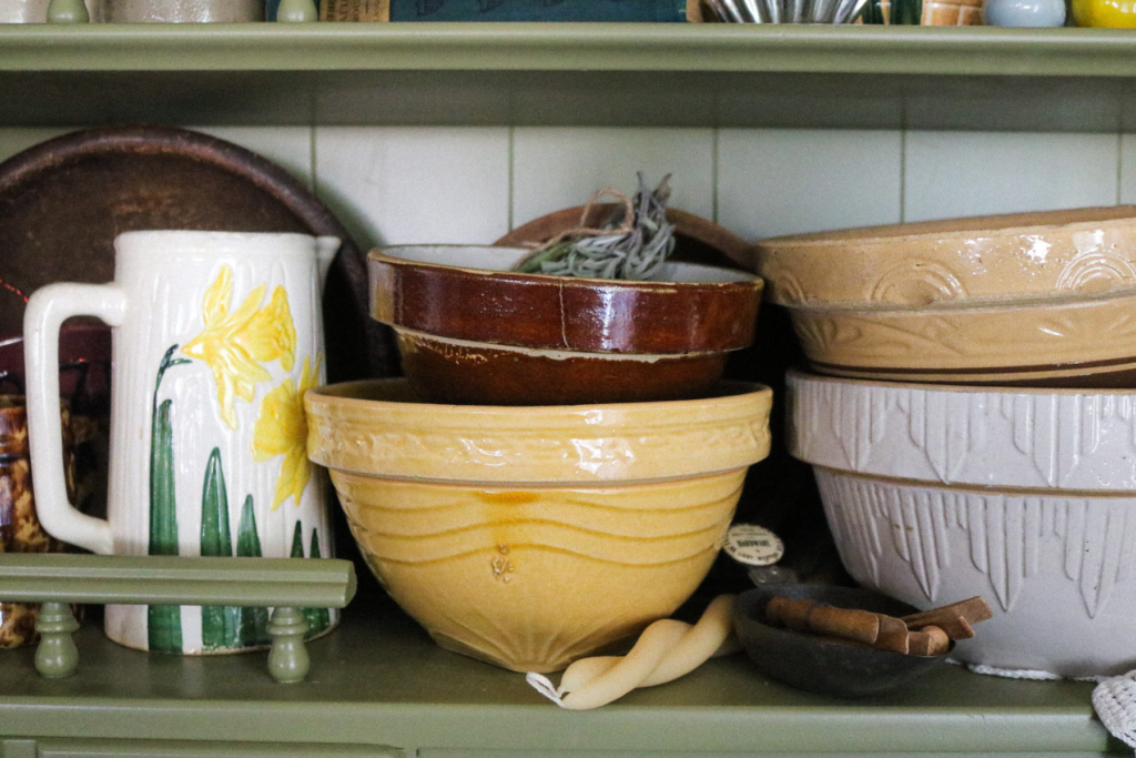 image of an antique stoneware vase with daffodils next to stoneware bowls stacked in a green hutch.