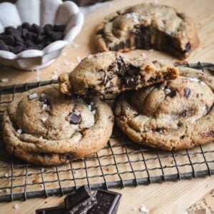 close up view of two thick brown butter chocolate chip cookies with half a cookie resting on top to show the texture and melted chocolate chips.