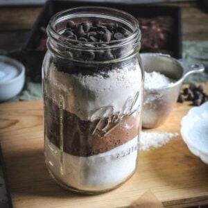 a wide mouth quart mason jar filled with the dry ingredients to make homemade brownies with a tray of homemade brownies in the background.